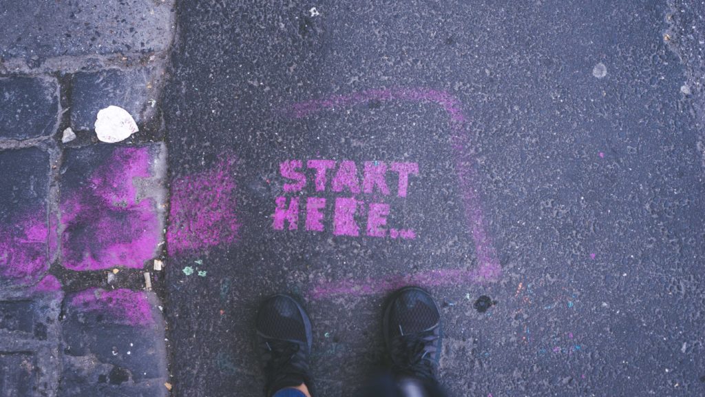 Starting a PhD: Grafitti on asphalt reading "Start here" with shoes in front of it, perspective from top