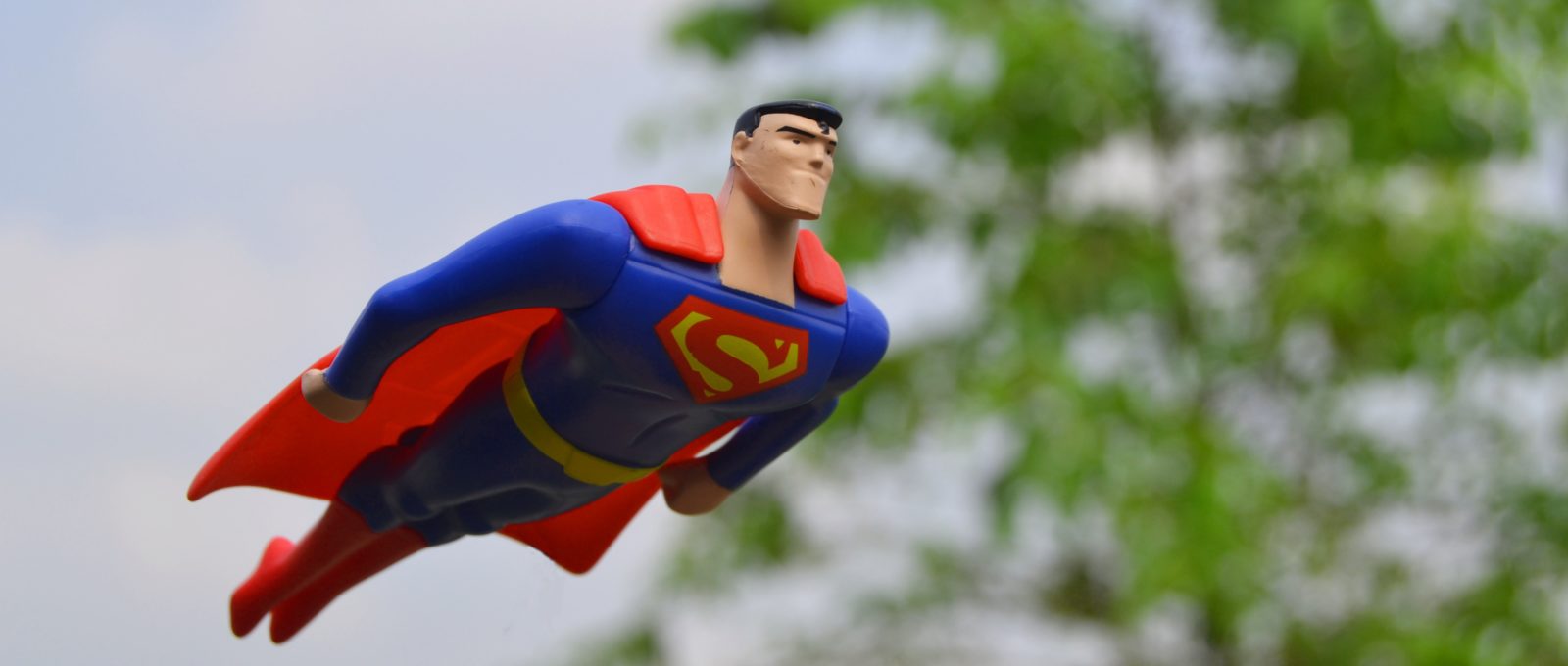 Superman Figure flying in front of green tree in blurry background