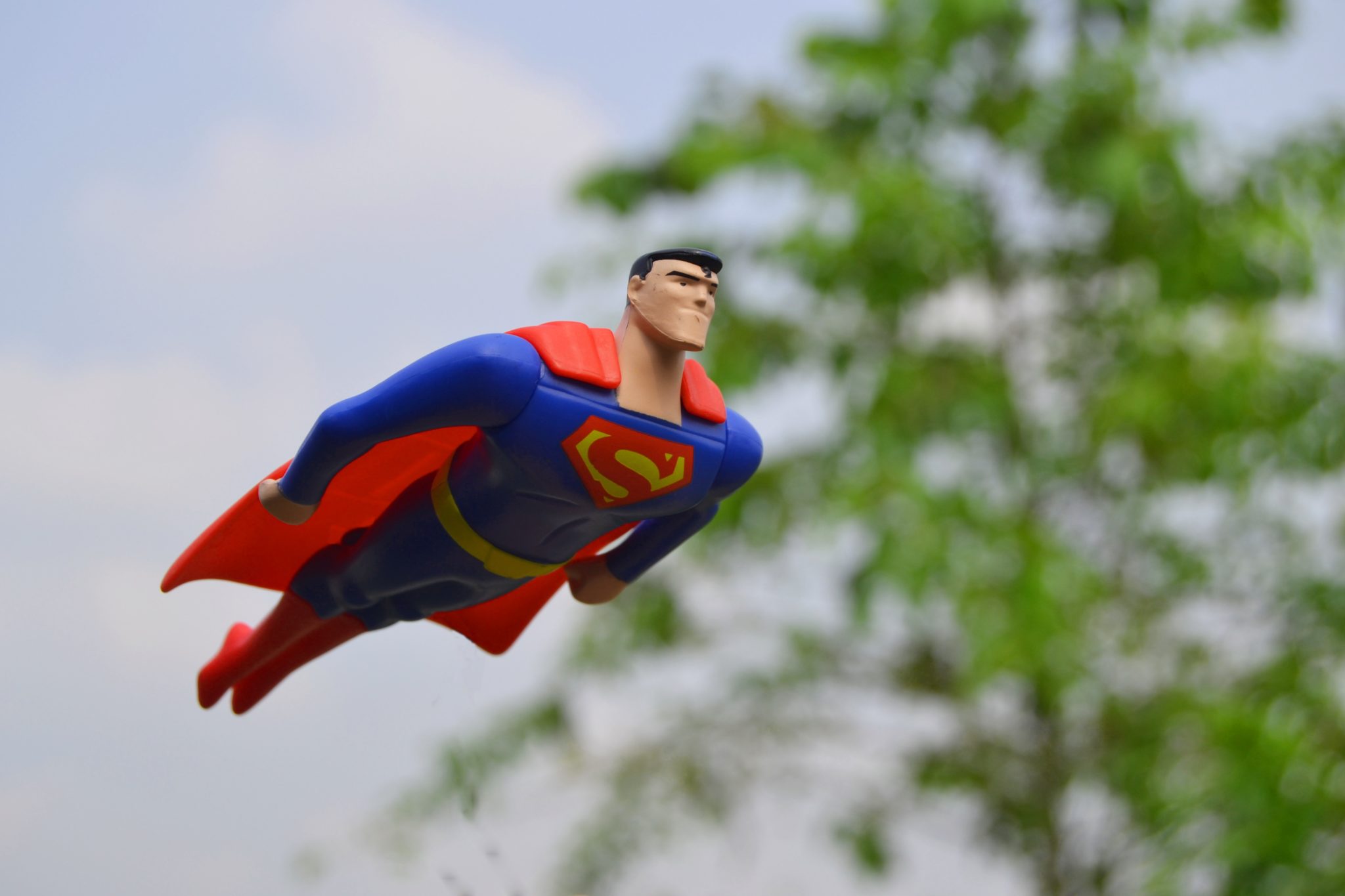 Superman Figure flying in front of green tree in blurry background